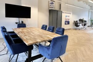 Vergaderruimte met houten tafel, blauwe stoelen en scherm in modern kantoor aan de Paulus Potterstraat.